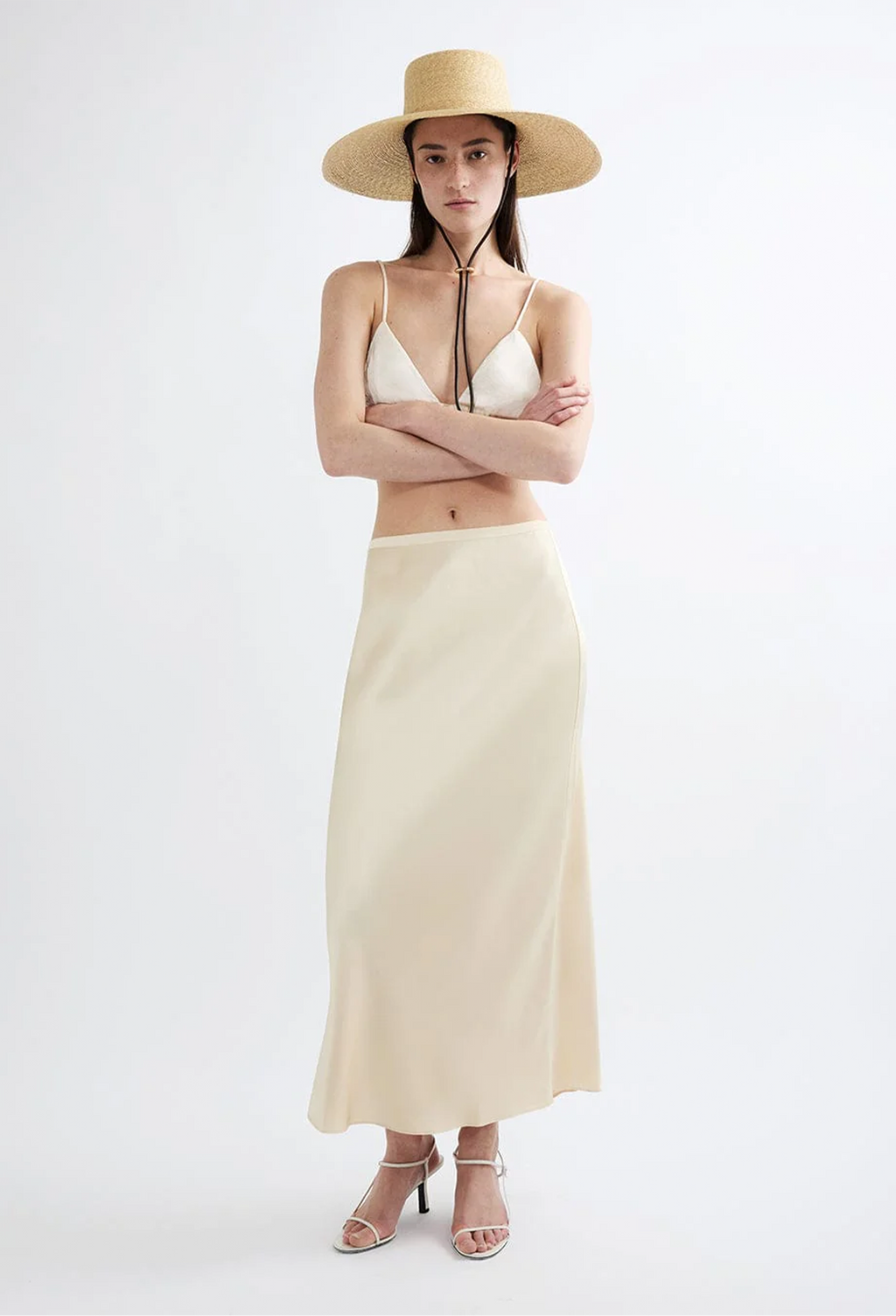 Woman wearing a beige hat, white top, and long beige skirt on a white background