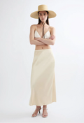Woman wearing a beige hat, white top, and long beige skirt on a white background