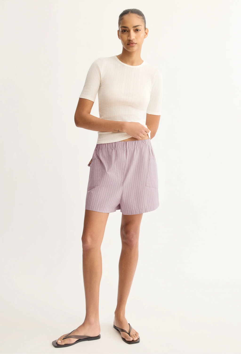 Woman wearing a white top and striped shorts on a plain background
