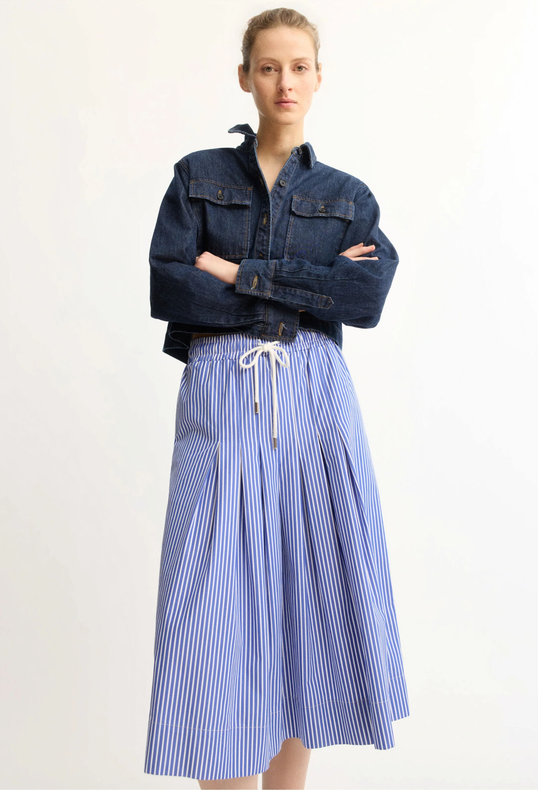 Woman wearing a denim jacket and blue striped skirt on a white background