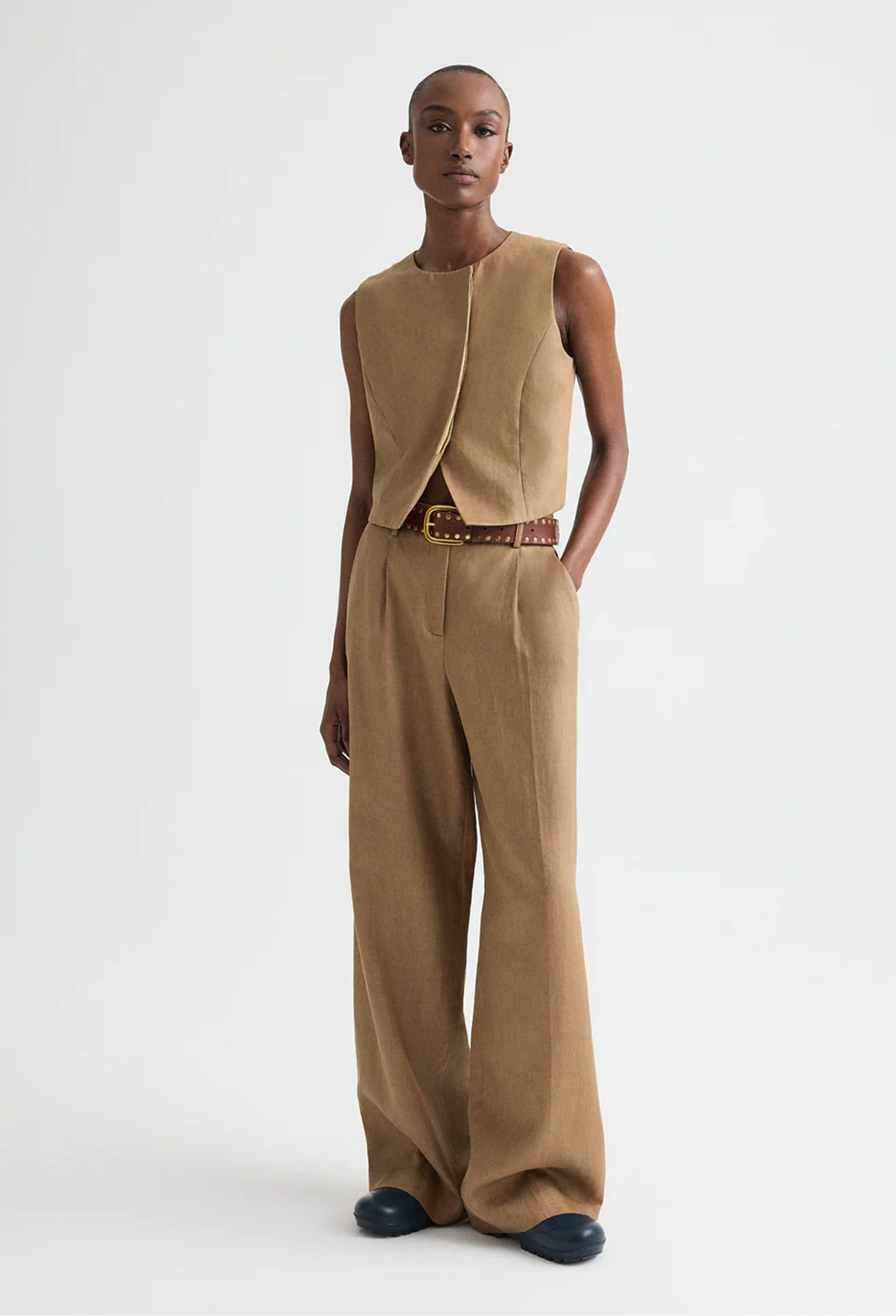 Person wearing a beige sleeveless top and wide-leg pants on a white background