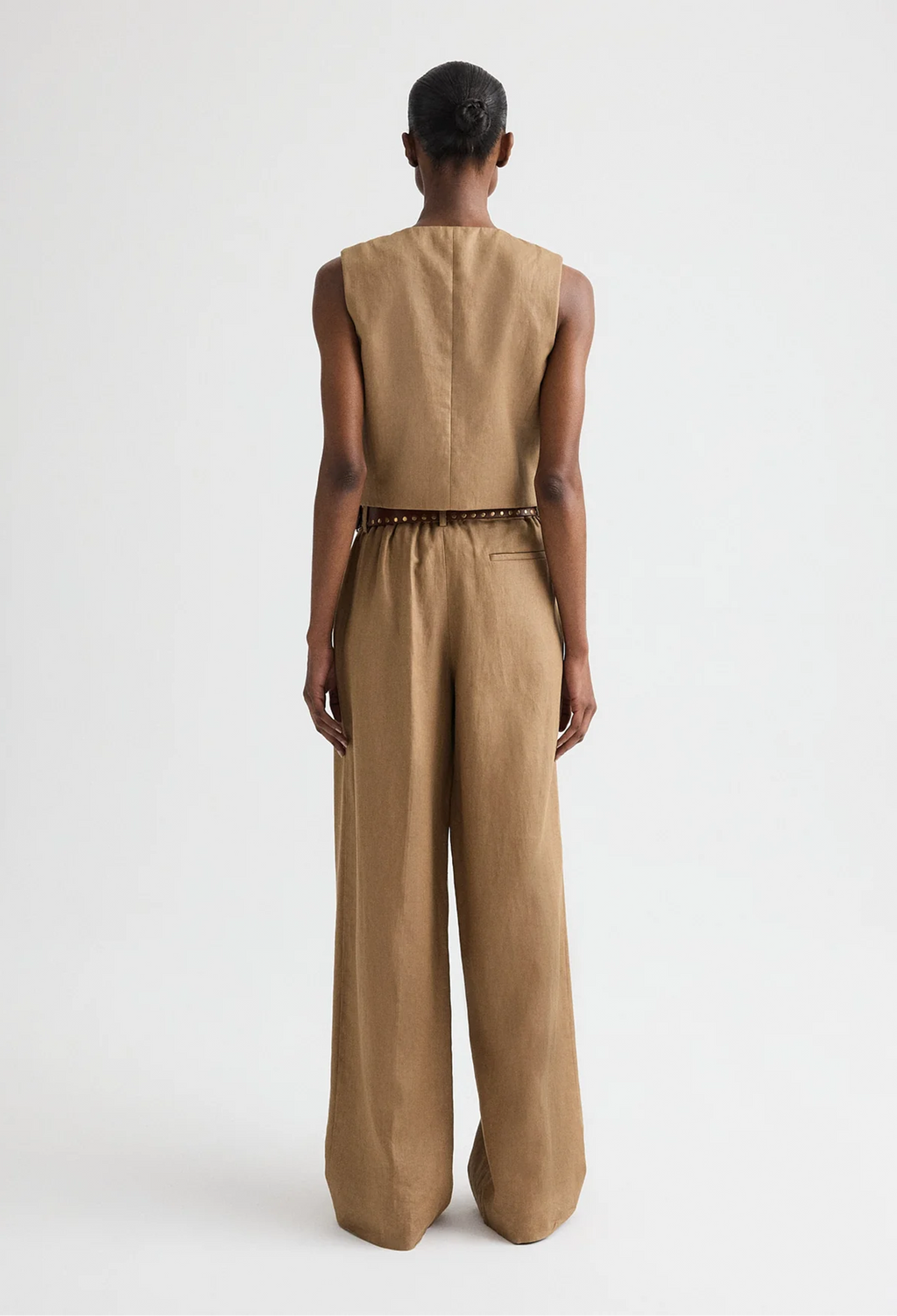 Person wearing a beige sleeveless top and wide-leg pants on a white background