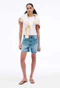 Woman wearing a white t-shirt, blue denim shorts, and a yellow cardigan on a white background