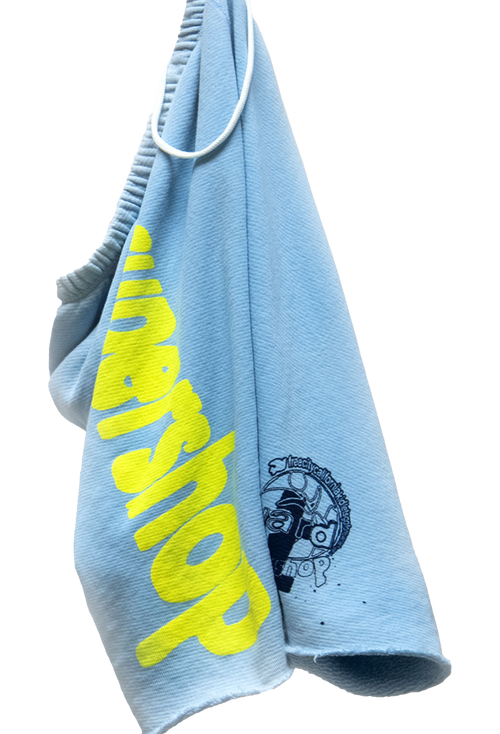 Light blue cutoff shorts with yellow text and black logo on a white background