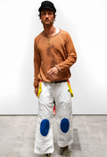 Man wearing a brown sweater and white pants with blue patches against a plain background