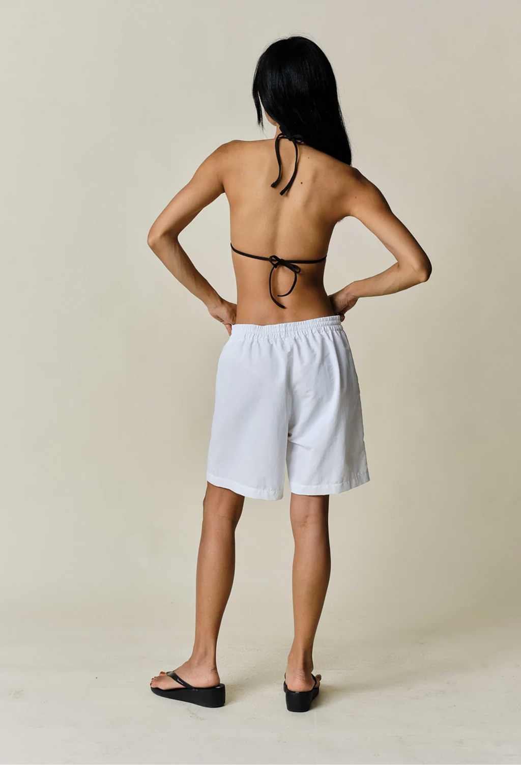a model wearing white shorts with a drawstring waist on a beige background