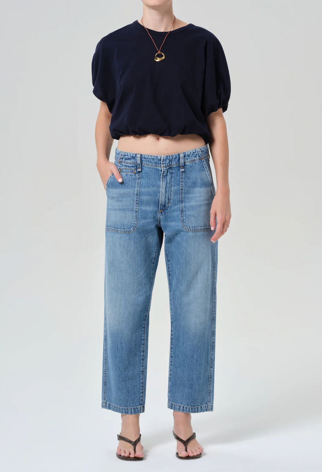 model wearing a blue top and jeans on a white background
