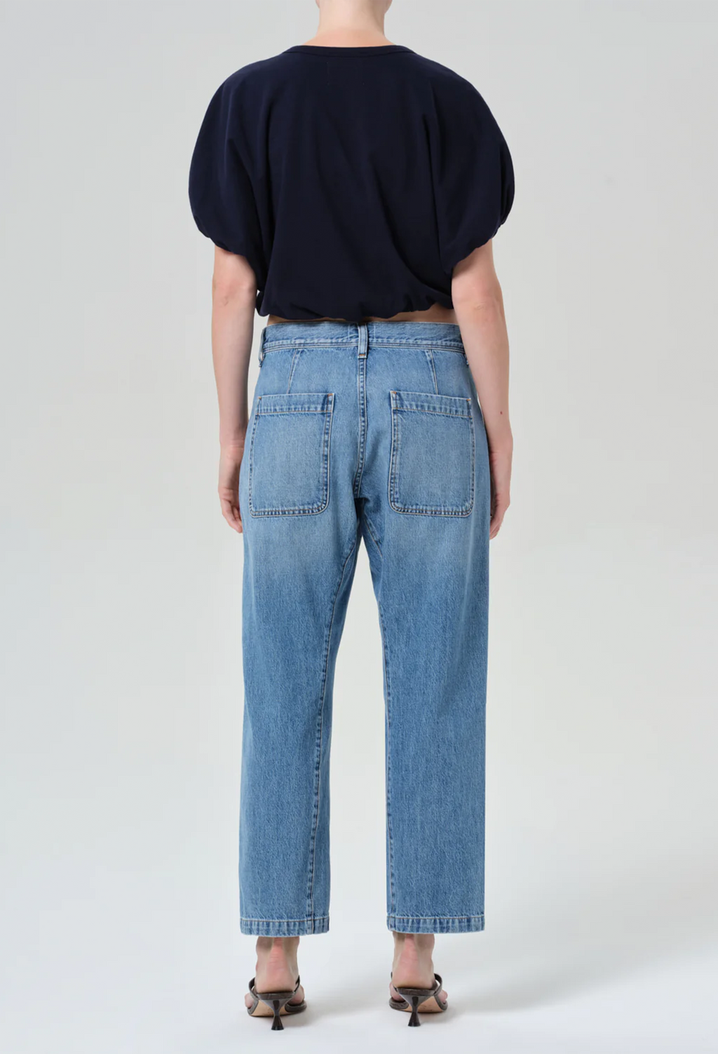 model wearing a blue top and jeans on a white background
