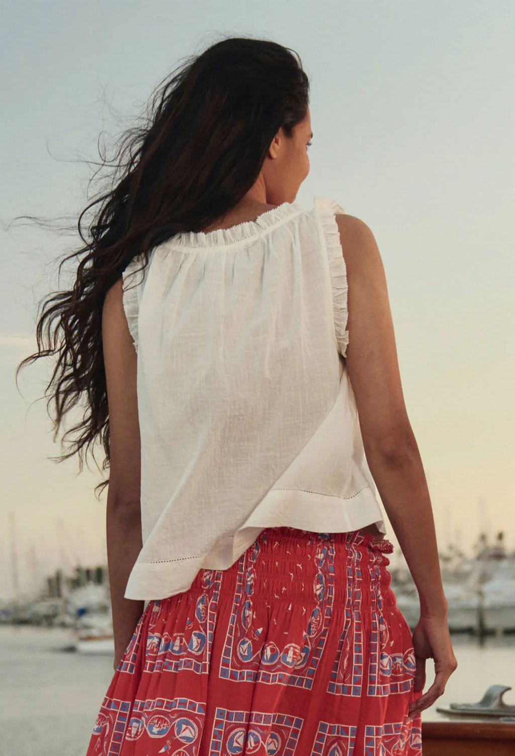 model wearing a sleeveless white button down top with ruffles on a boat
