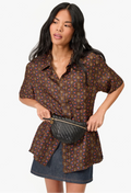 Woman wearing a patterned shirt and denim skirt holding a black handbag on a white background