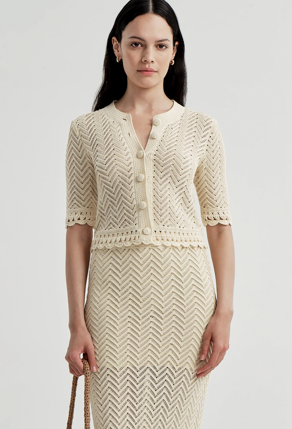 Woman wearing an off white crocheted outfit on a light gray background