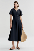 Woman wearing a navy dress holding a straw bag on a white background