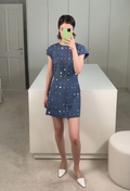 Person wearing a blue dress with colorful polka dots in a minimalistic room.