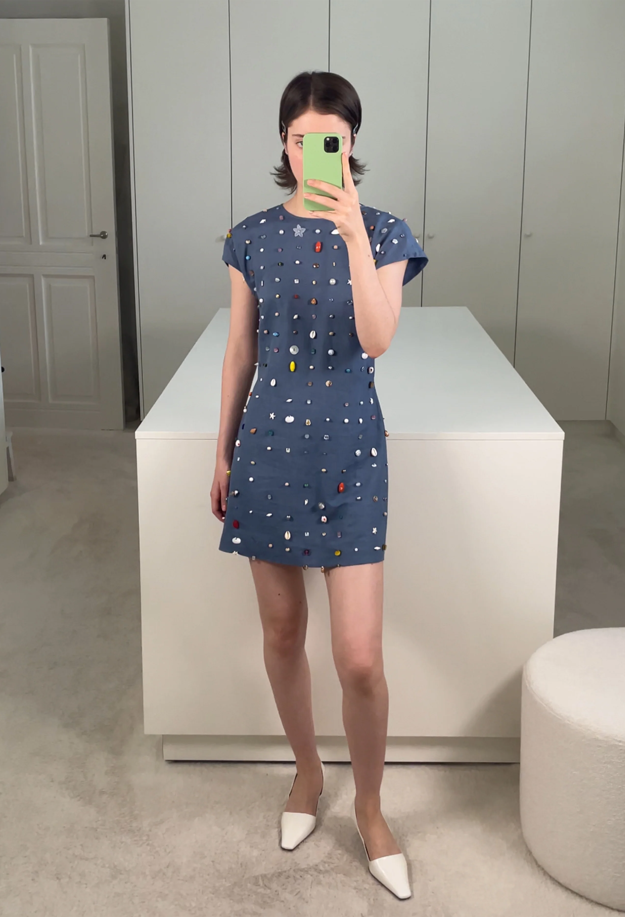 Person wearing a blue dress with colorful polka dots in a minimalistic room.