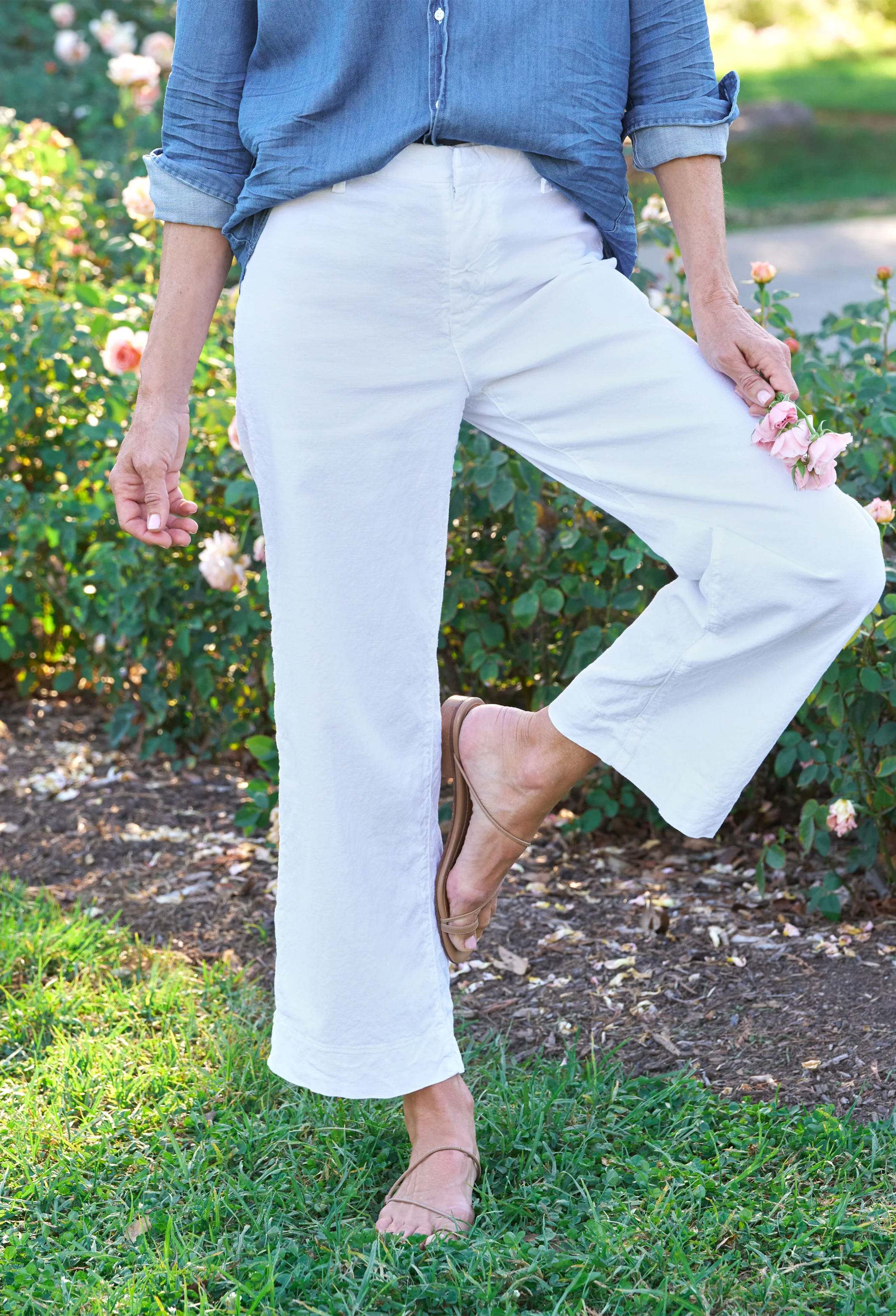 Person wearing white pants and a blue shirt standing in a garden.