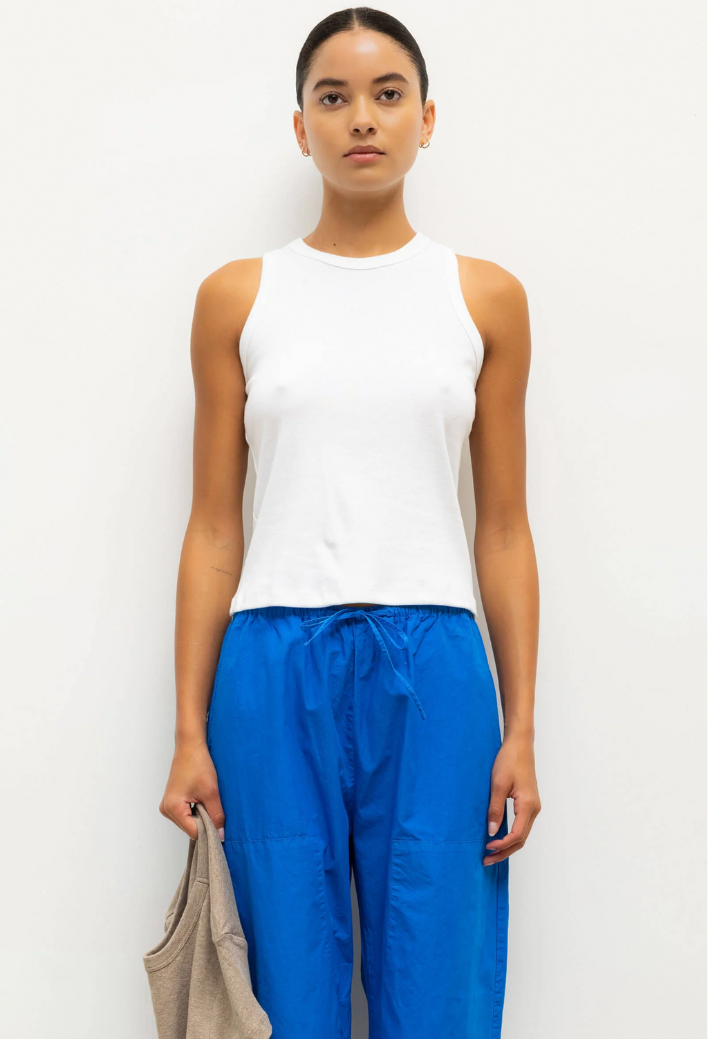 Woman wearing a white sleeveless top and blue pants against a white background