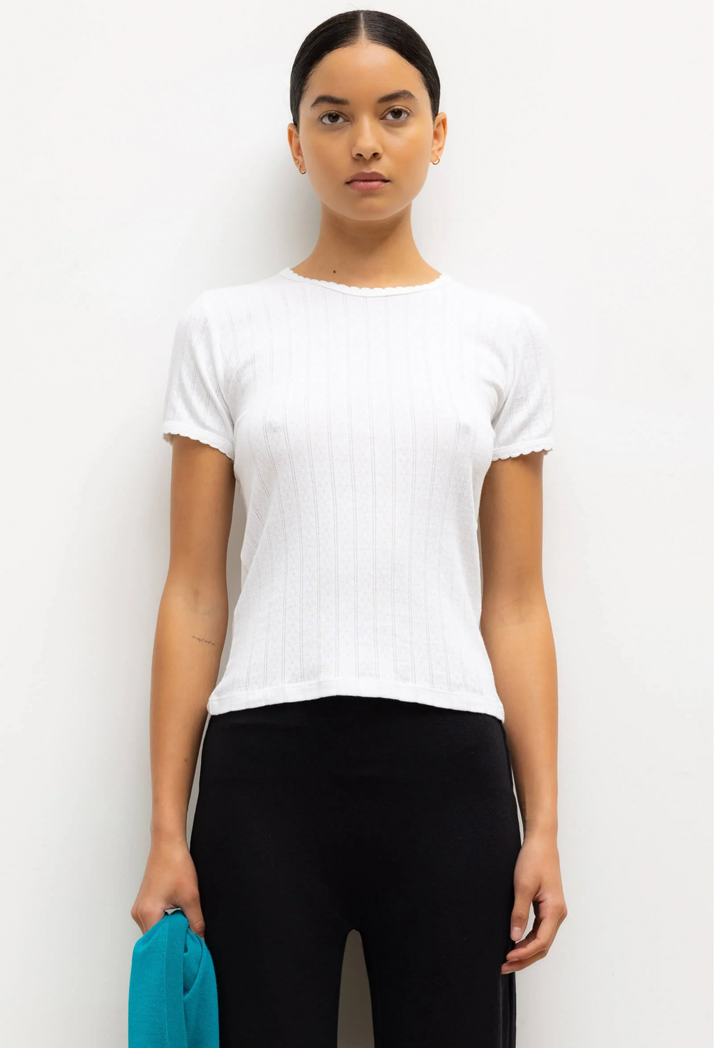 Woman wearing a white t-shirt and black pants holding a blue object against a white background