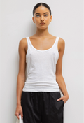 Woman wearing a white tank top and black pants against a light gray background