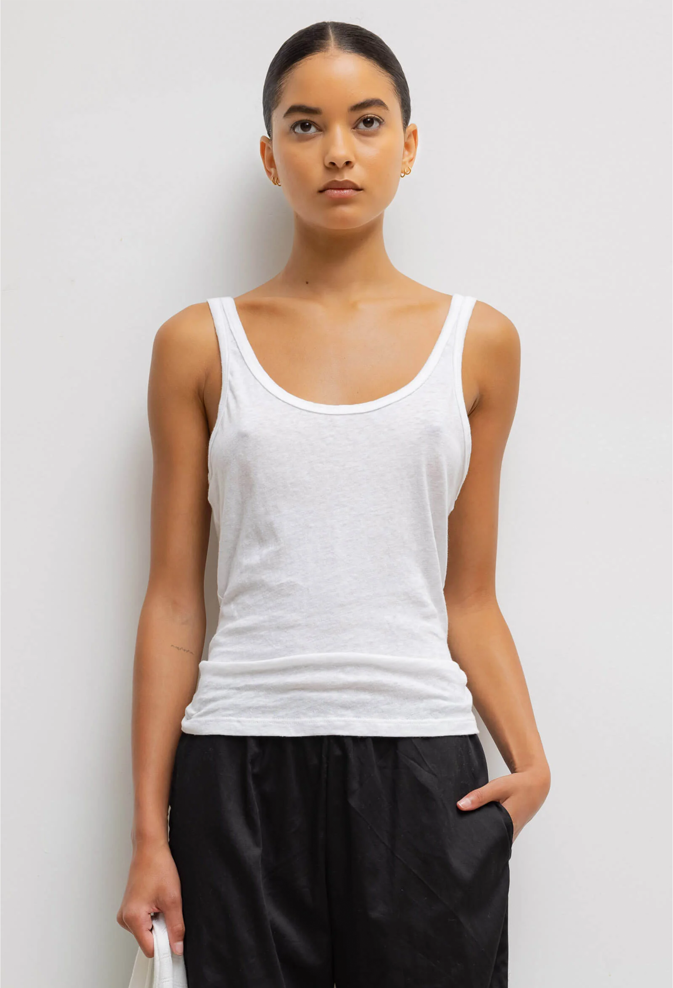 Woman wearing a white tank top and black pants against a light gray background