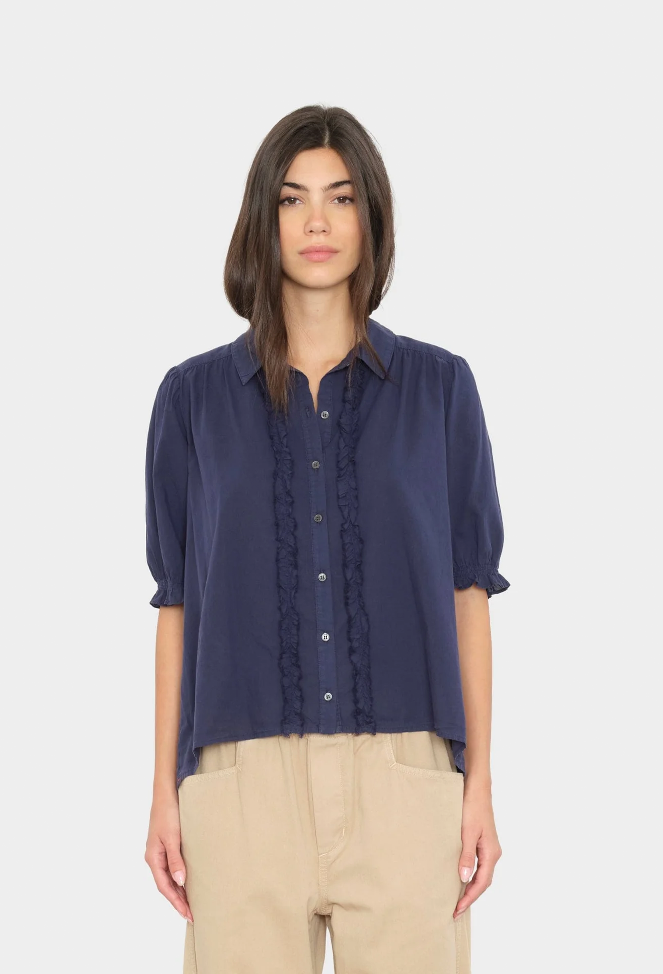 Woman wearing a navy blue blouse with ruffled details on a white background