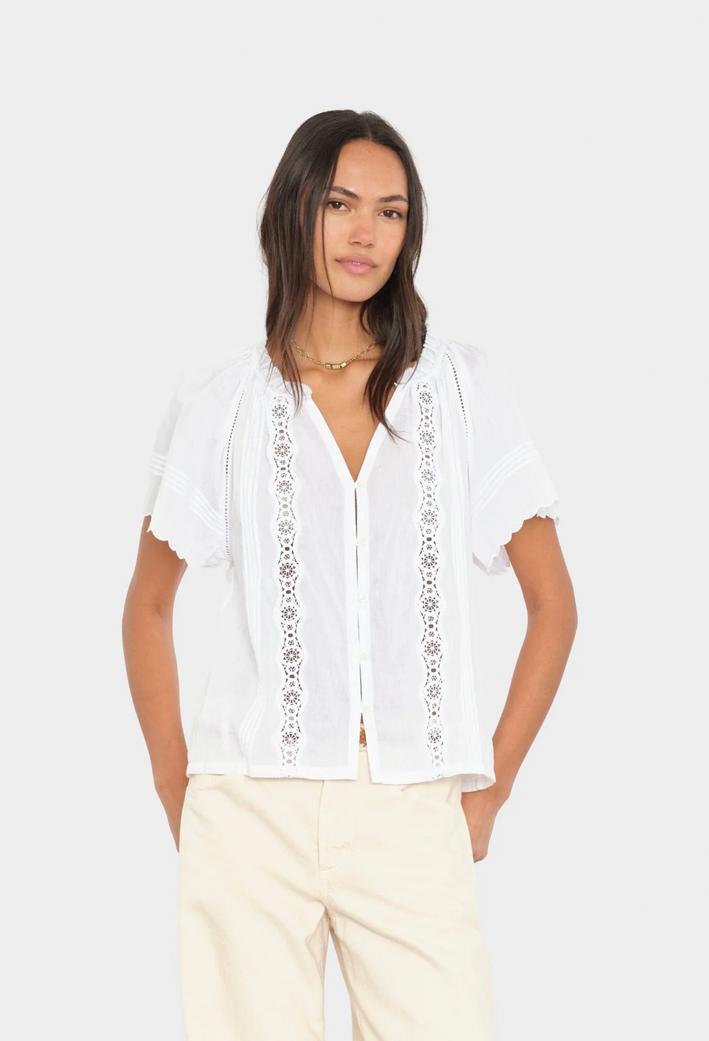 Woman wearing a white blouse with lace details on a plain background