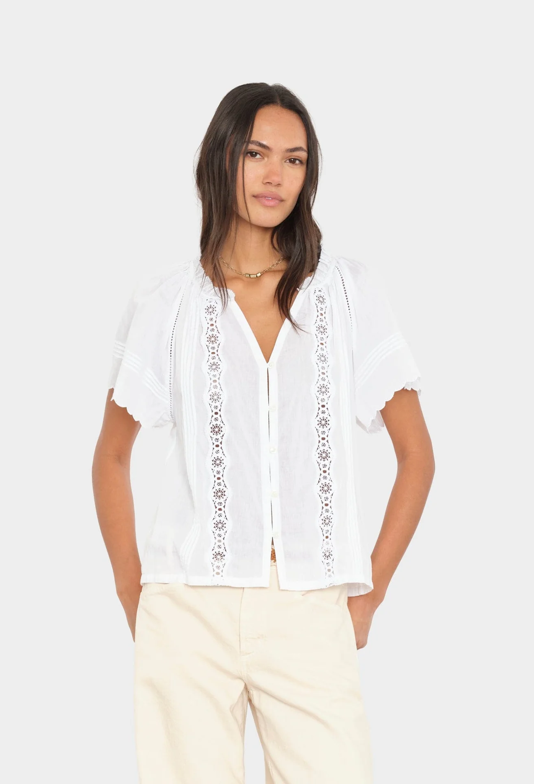 Woman wearing a white blouse with lace details on a plain background