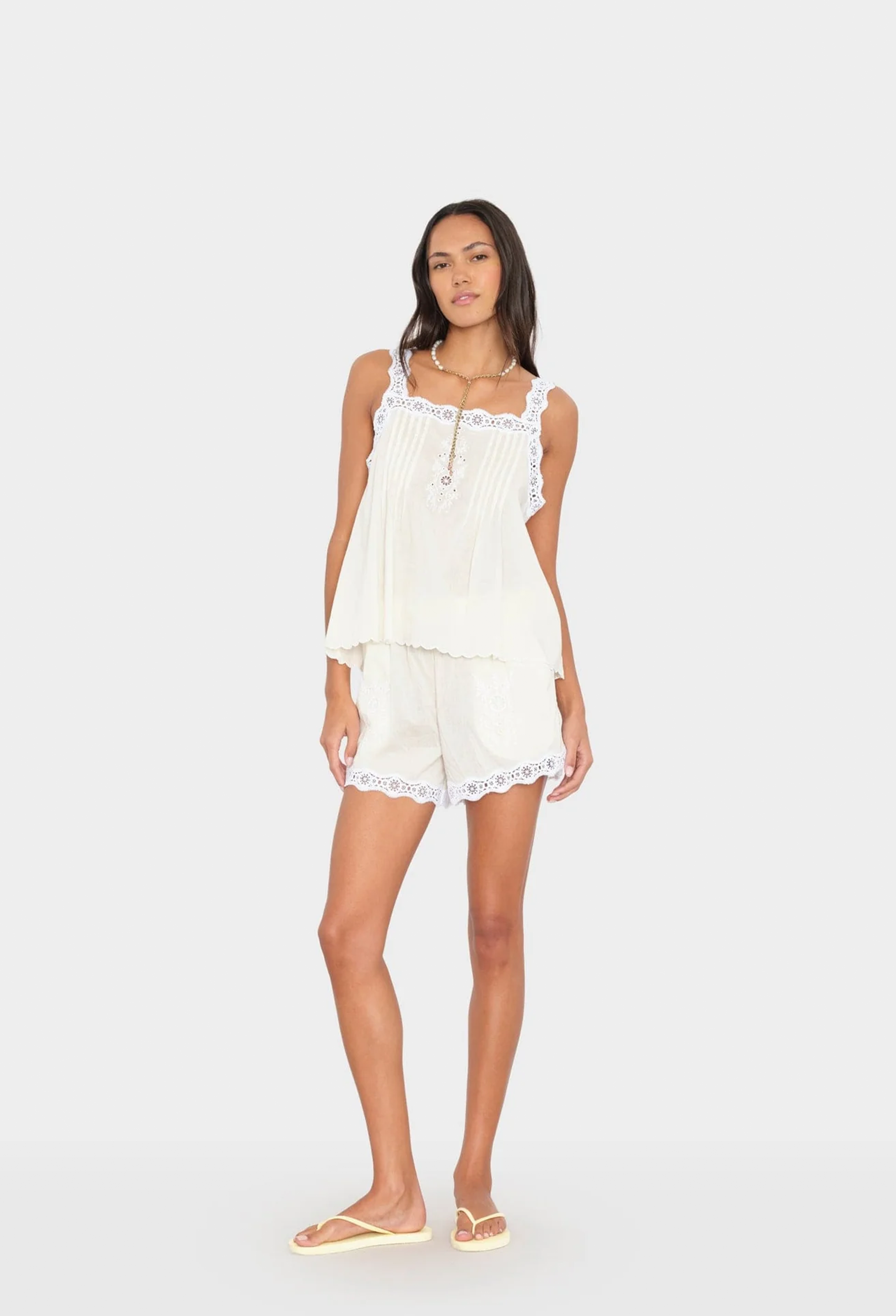 Woman wearing a white lace-trimmed top and shorts set on a white background