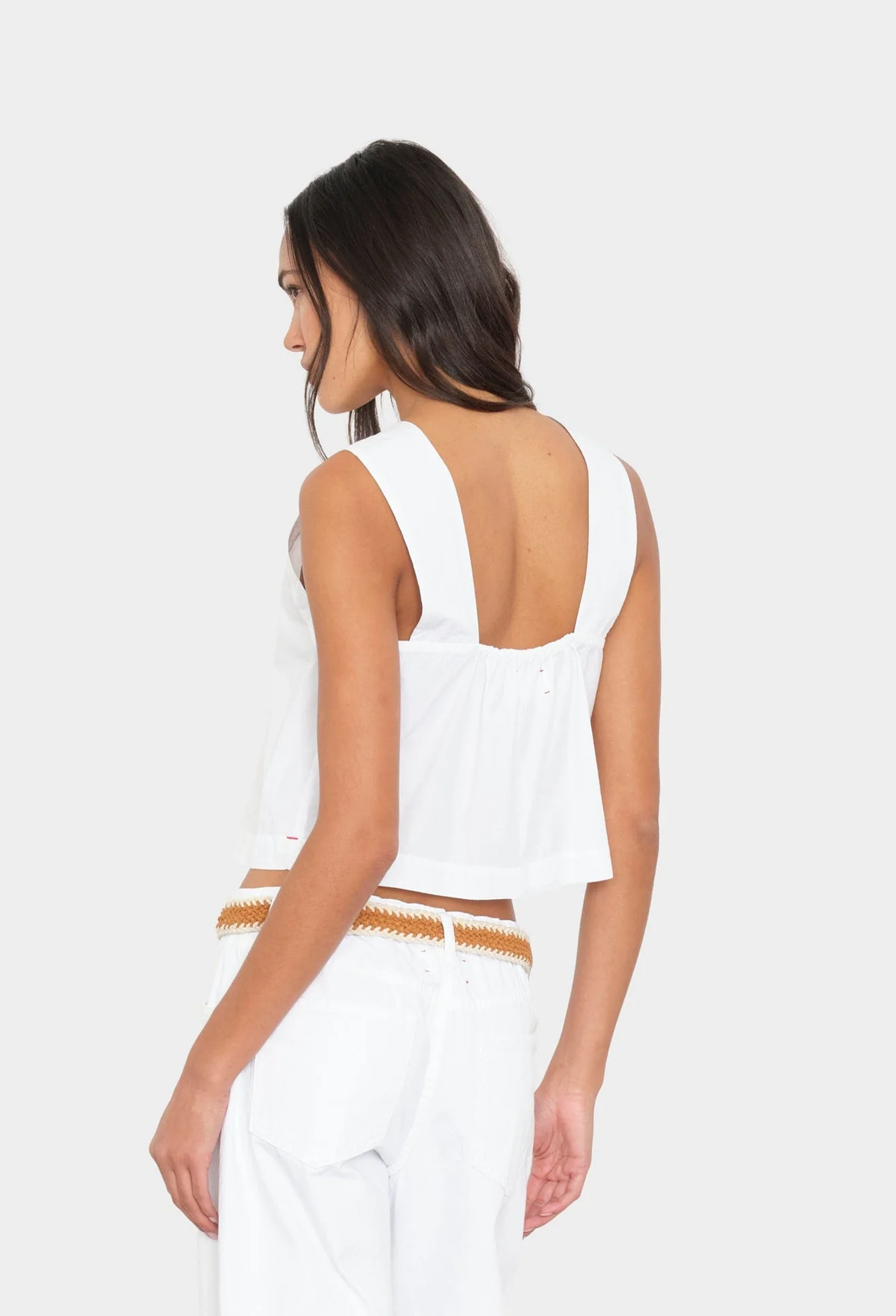 Woman wearing a white sleeveless top with a cutout design on a white background