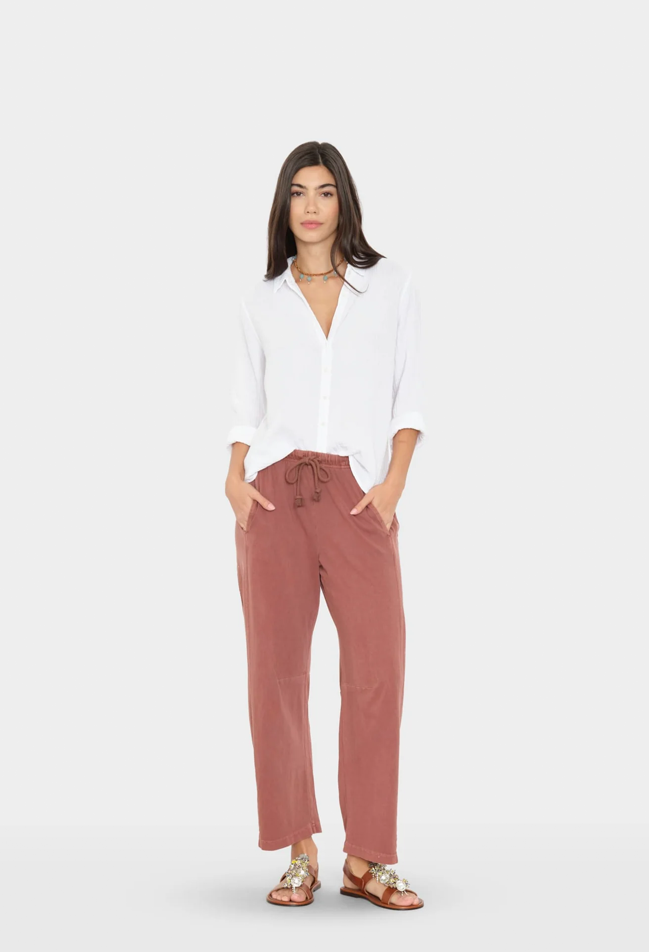 Woman wearing a white blouse and faded red pants on a white background