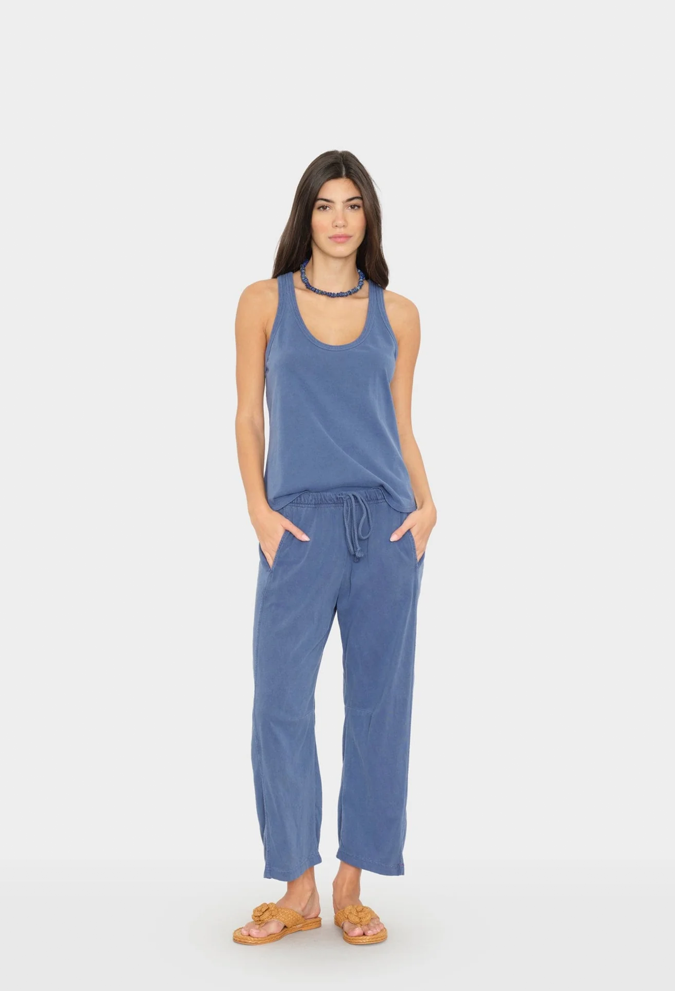 Woman wearing a blue sleeveless top and pants on a white background