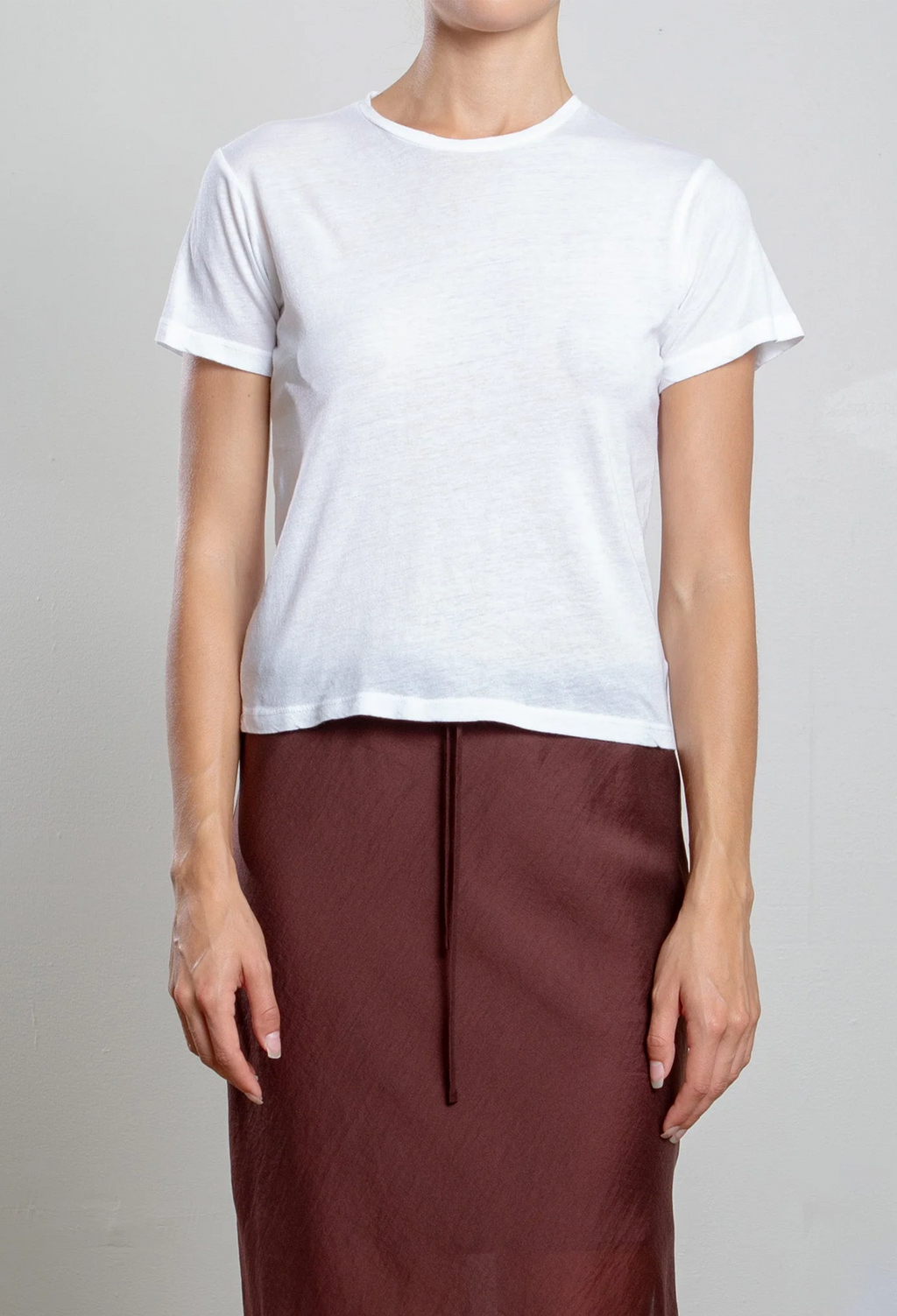 Person wearing a white t-shirt and brown skirt on a plain background