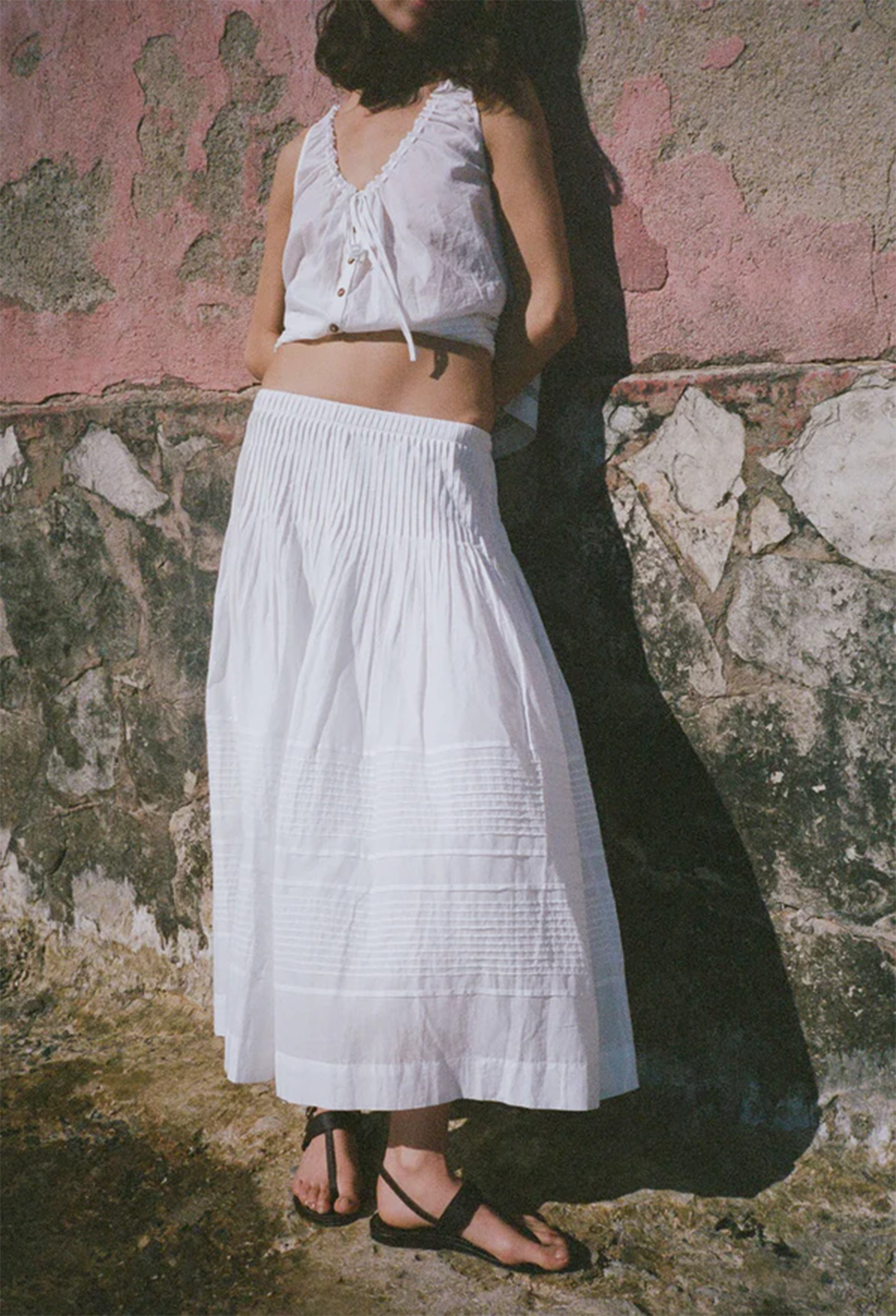 Person wearing a white outfit standing against a textured wall.
