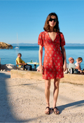 Woman in a red dress standing by the sea with people in the background