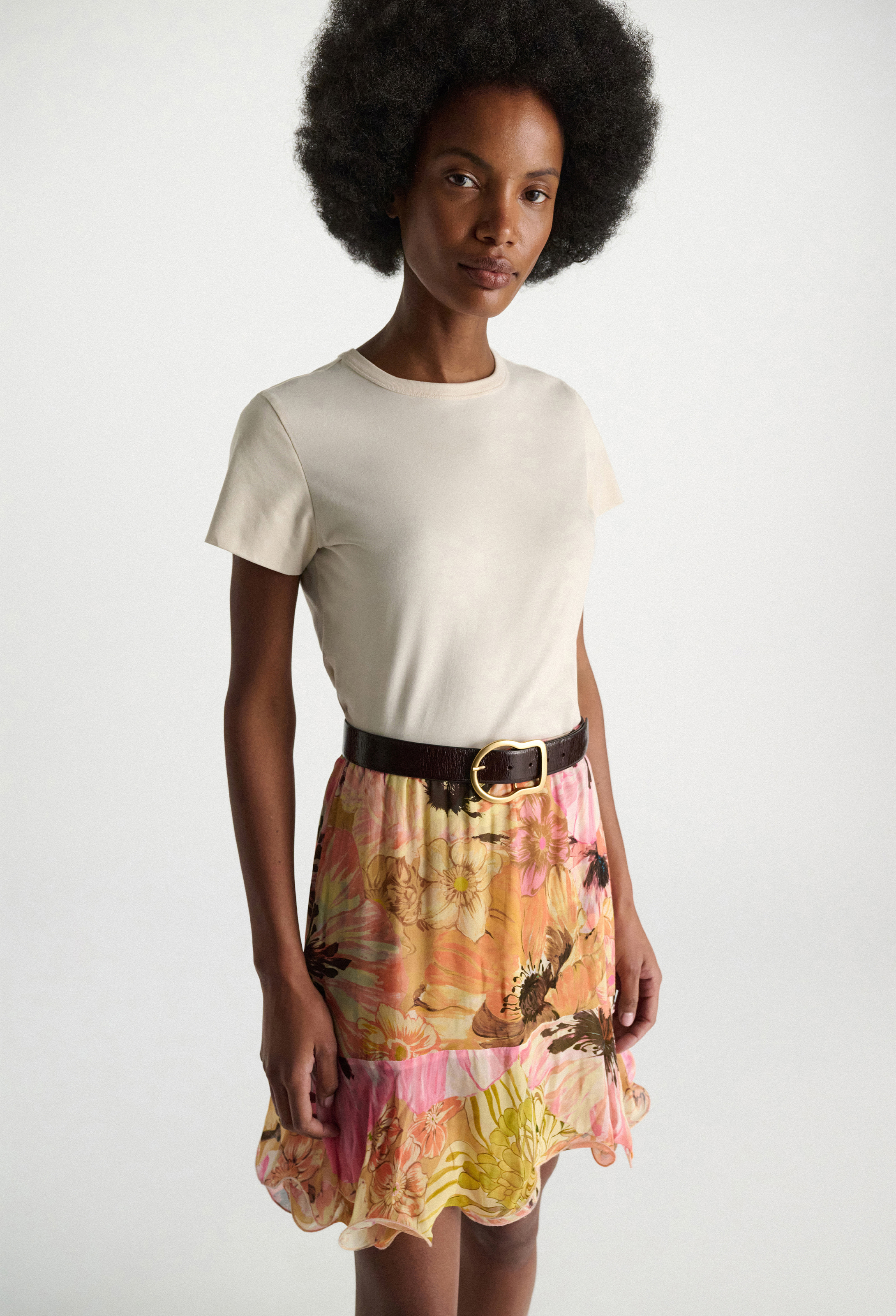 Woman wearing a white t-shirt and colorful floral skirt on a plain background