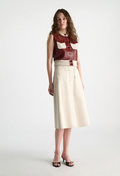 Woman wearing a sleeveless top with a unique button design and a cream skirt on a white background
