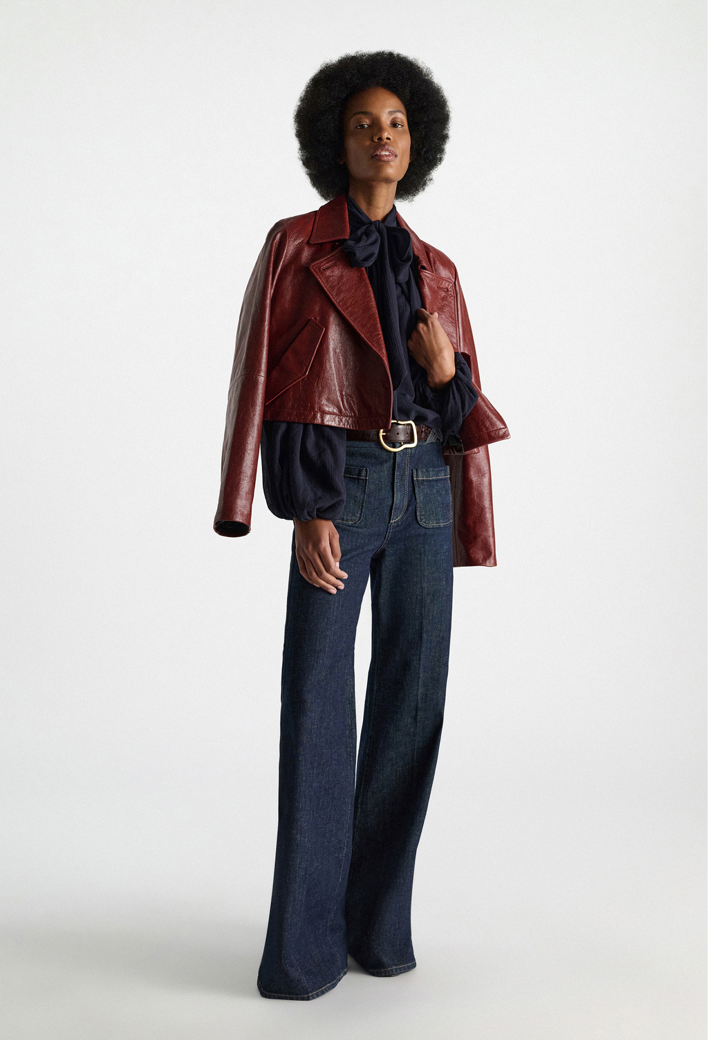 Person wearing a red leather jacket, black shirt, and blue jeans on a white background