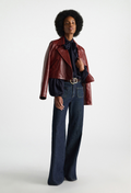 Person wearing a red leather jacket, black shirt, and blue jeans on a white background