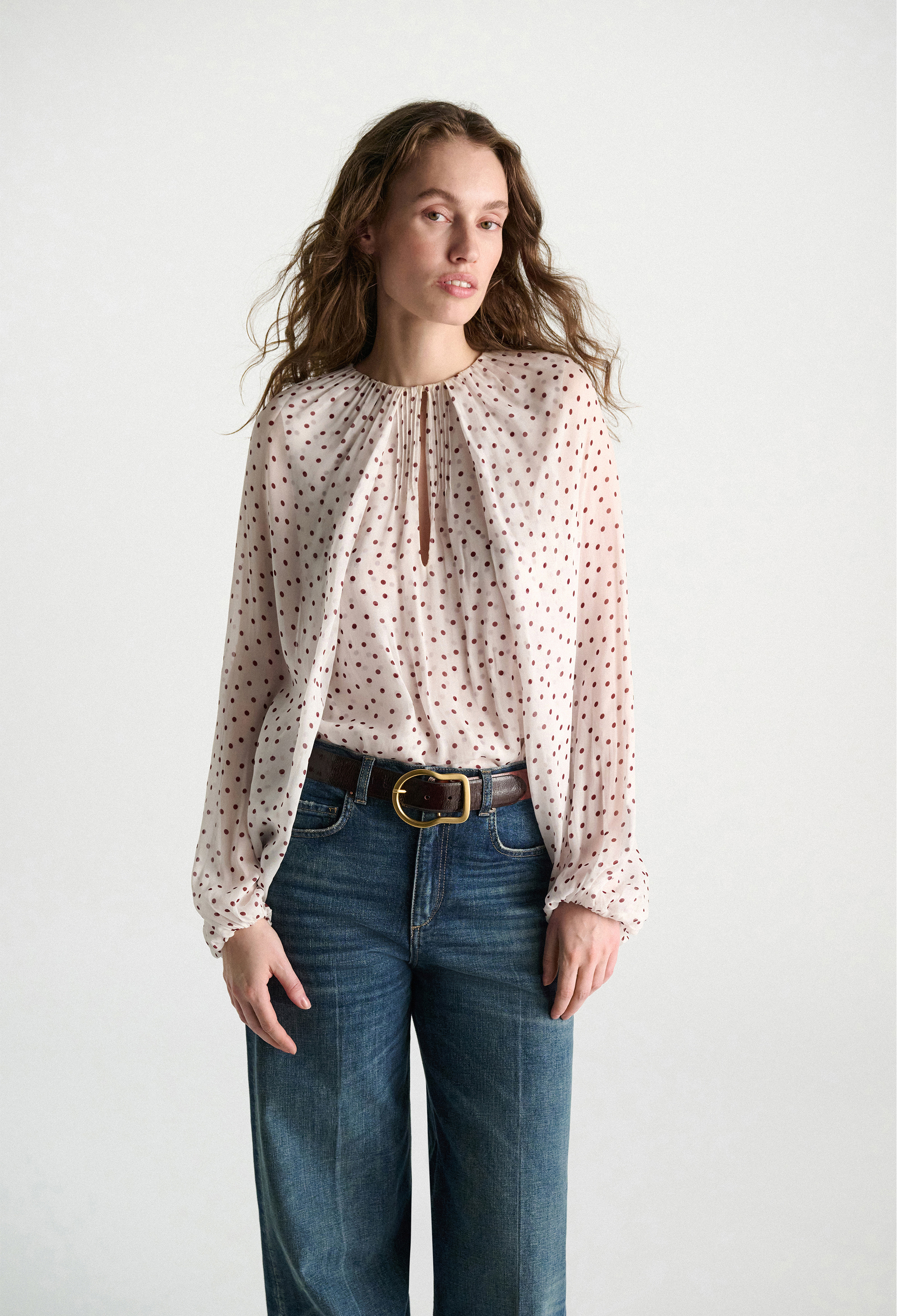 Woman wearing a polka dot blouse and blue jeans on a white background
