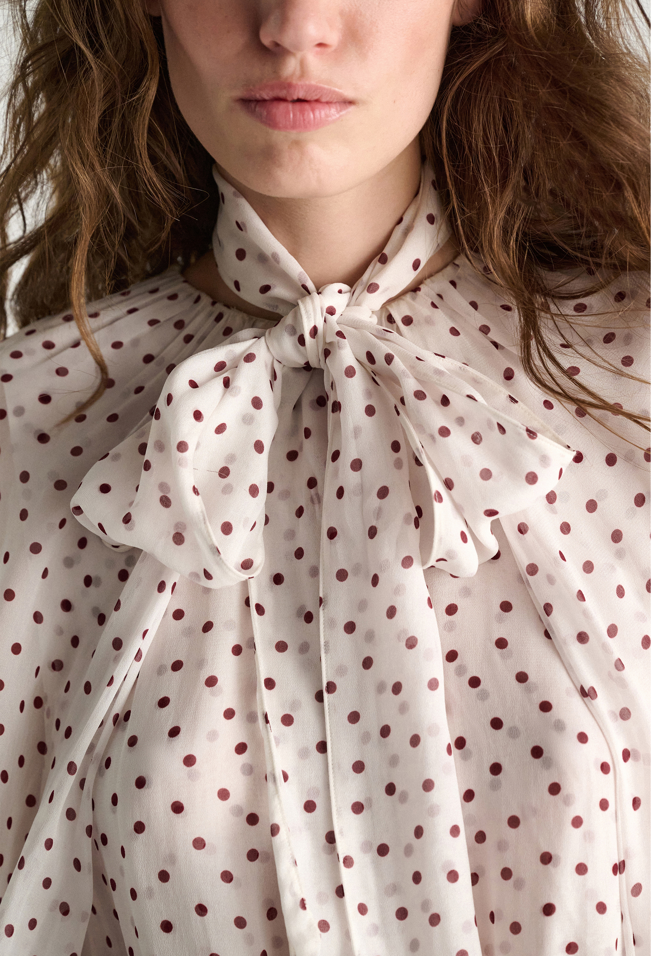Close-up of a person wearing a polka dot blouse with a bow neckline.