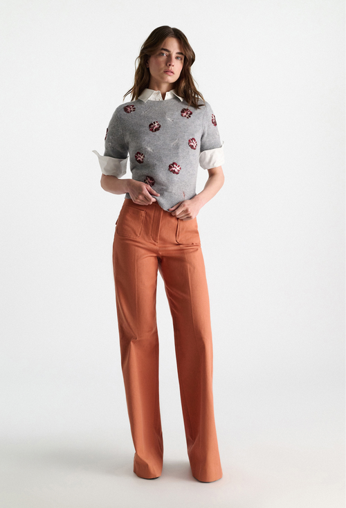 Woman wearing a patterned shirt and orange pants on a white background