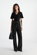 Woman wearing a black outfit with wide-leg pants on a white background