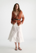 Woman wearing a rust-colored cardigan over a white dress on a white background