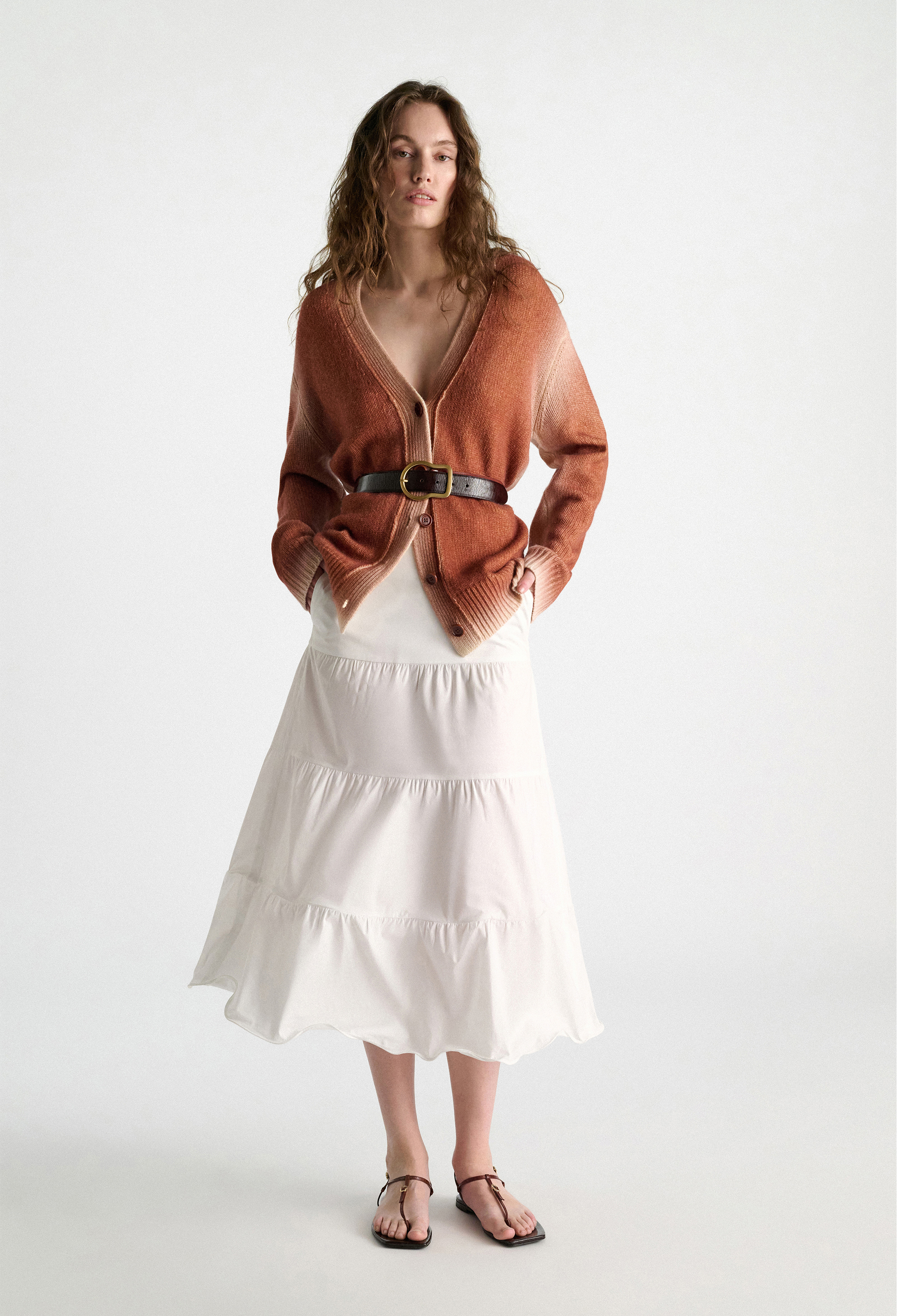Woman wearing a rust-colored cardigan over a white dress on a white background