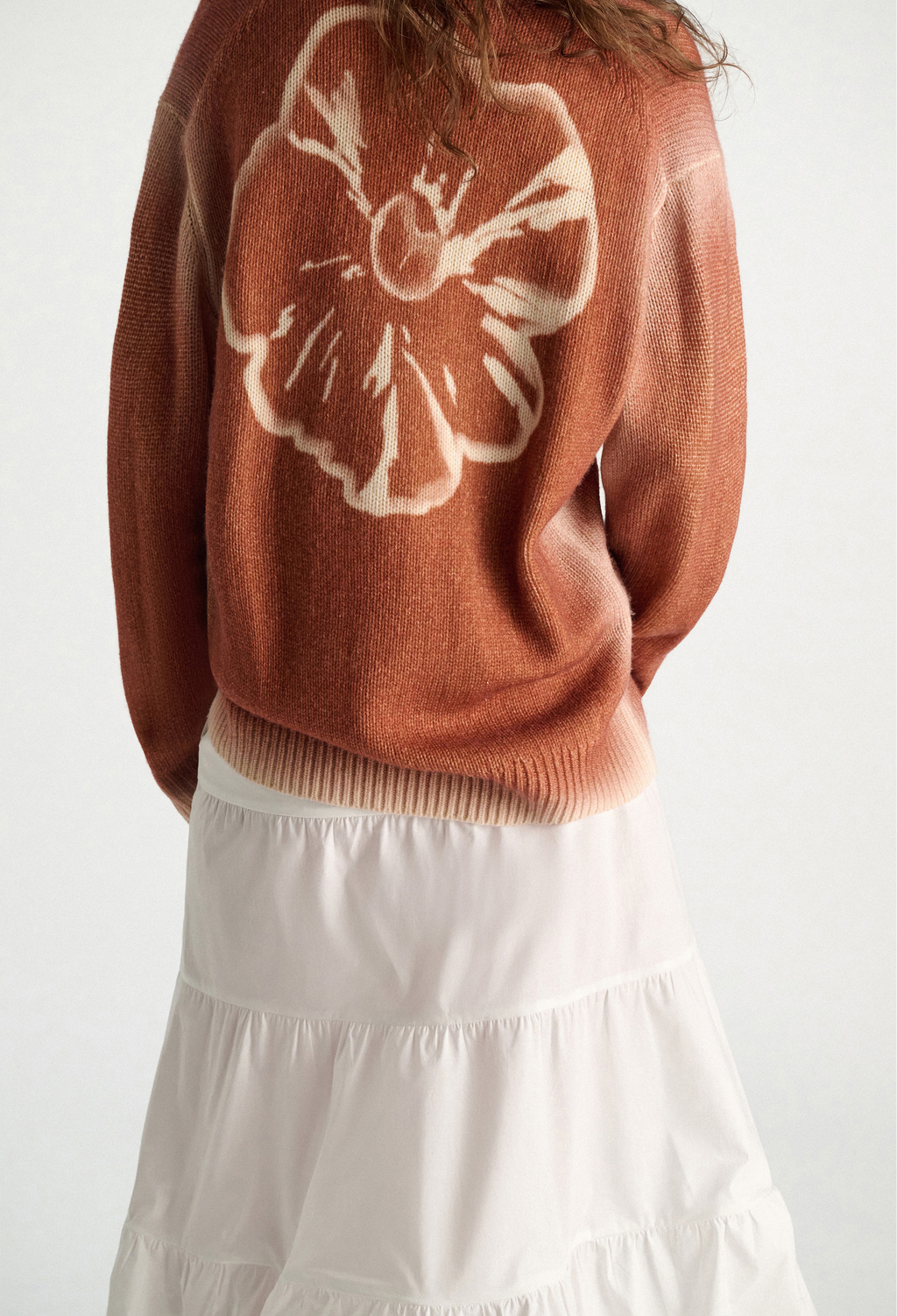 Person wearing a brown sweater with a white floral design on a white background