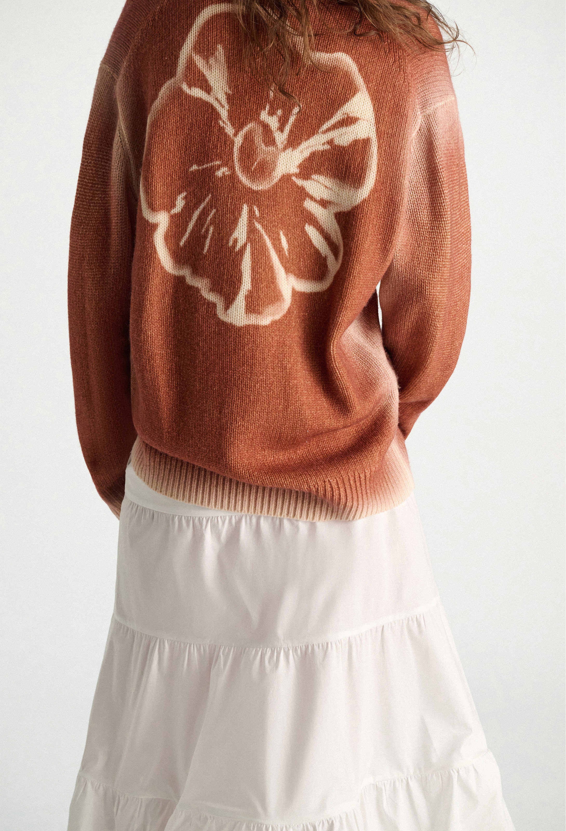 Person wearing a brown sweater with a white floral design on a white background