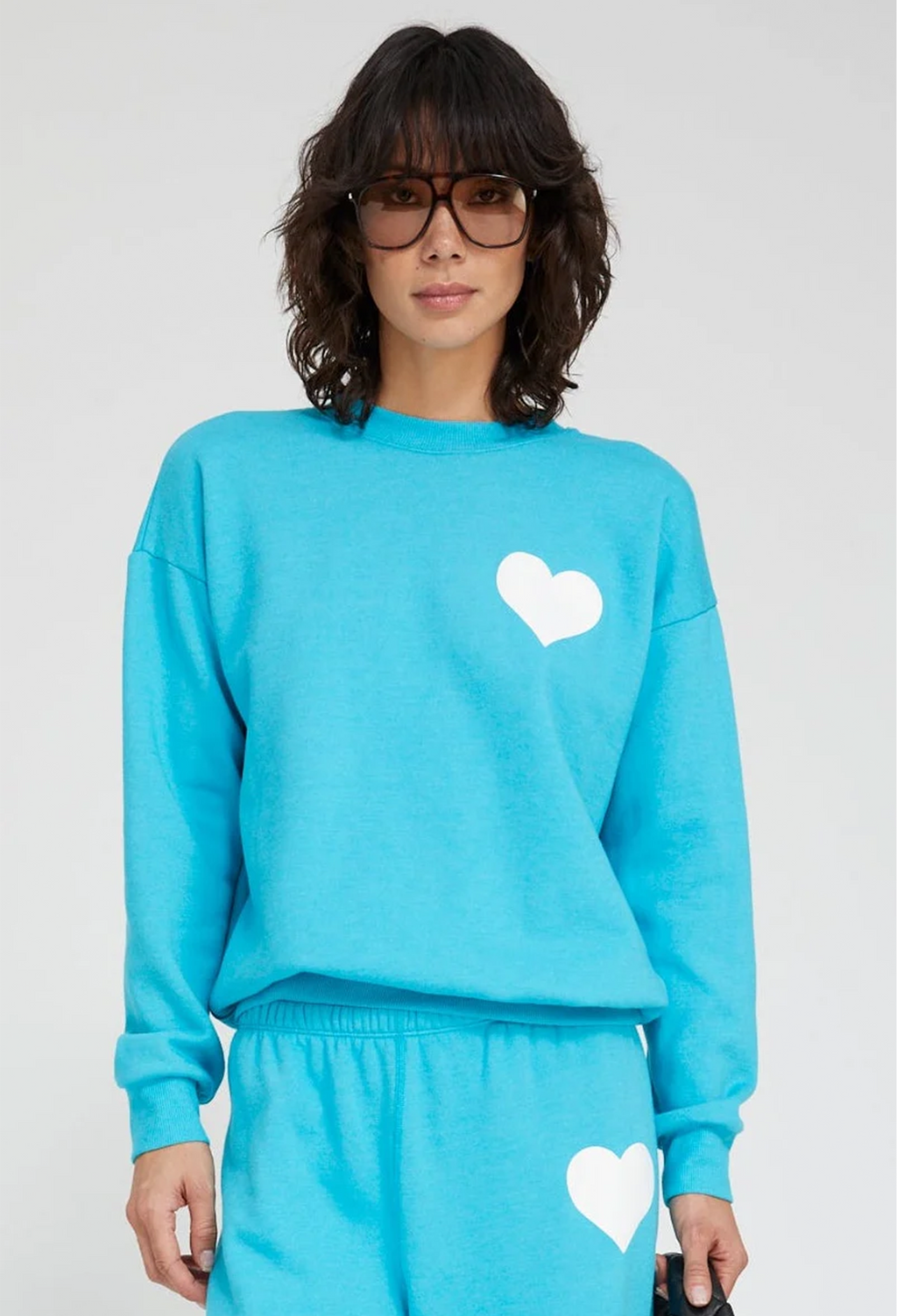 Person wearing a blue sweatshirt with a white heart design on a plain background