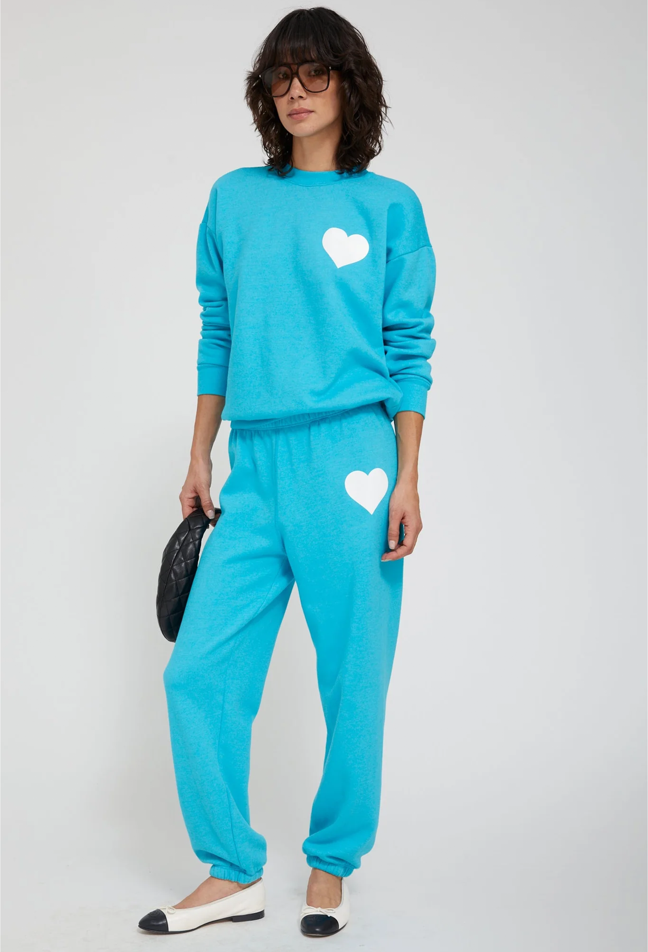 Person wearing a turquoise sweat suit with white hearts on a plain background