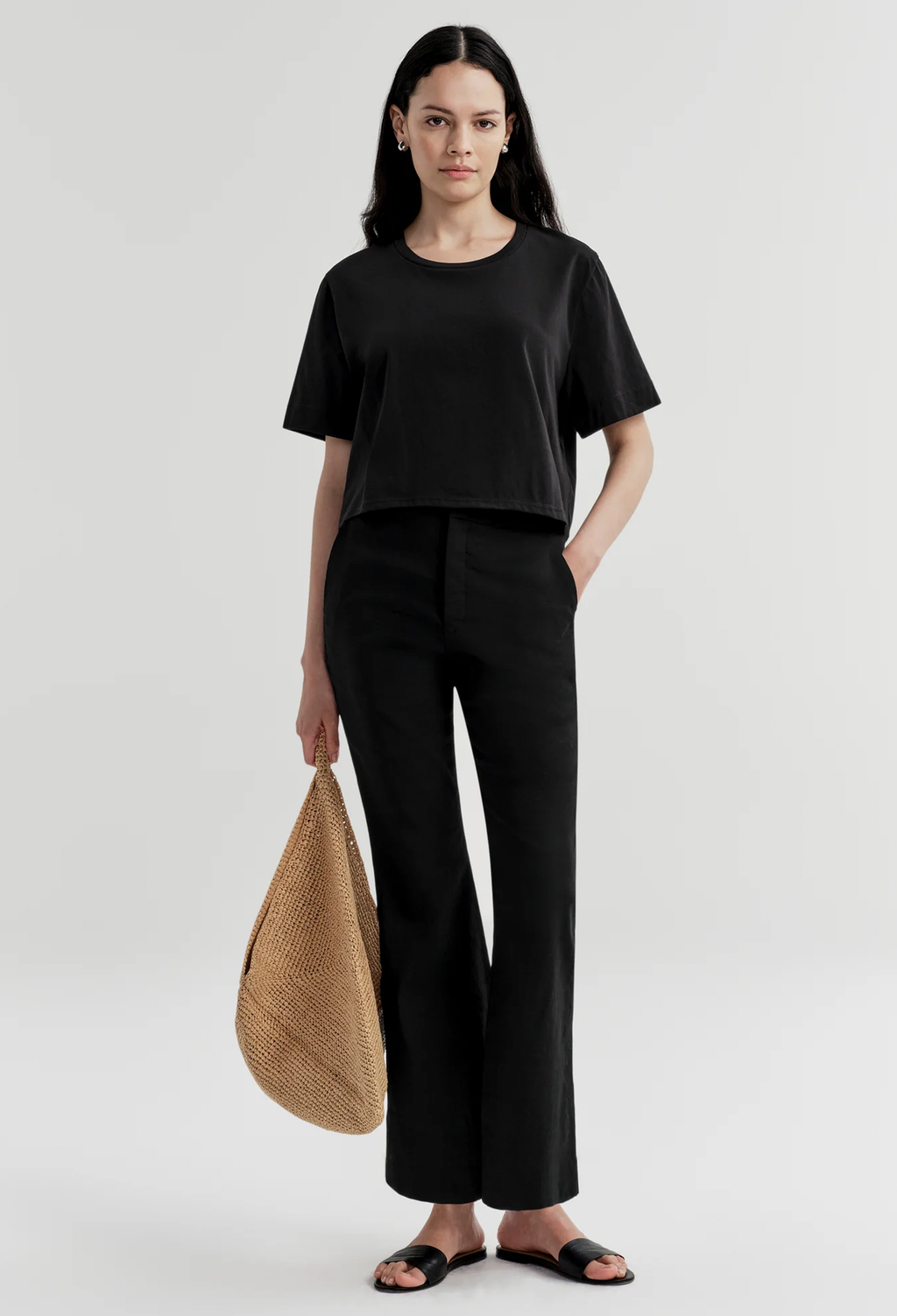 Woman wearing a black outfit holding a woven bag on a white background