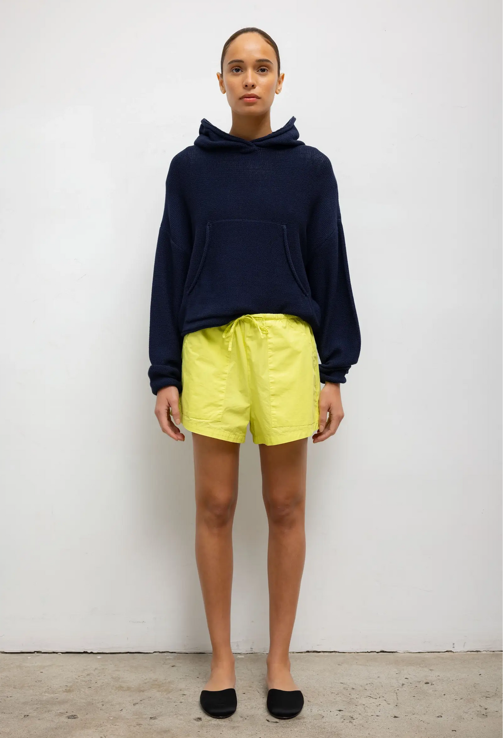 Person wearing a navy hoodie and yellow shorts against a white background