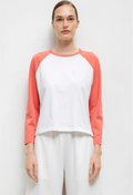 Person wearing a white and coral baseball shirt with white pants on a light gray background